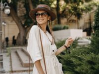 attractive woman walking in street on vacation dressed in white summer fashion dress straw hat and purse, smiling happy having fun, stylish accessories trend